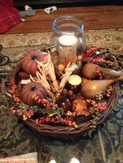 a woven tray with corn and corn husks, berries, faux pumpkins and pears plus a candle in the center