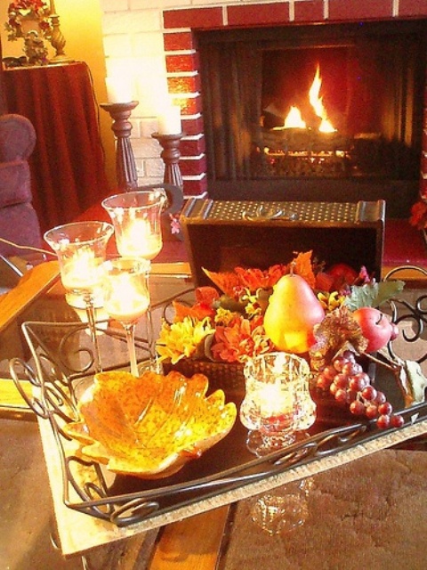 a fall coffee table with candles, a sivler tray with a leaf bowl and fake fruits that look rather natural