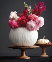 a white pumpkin used as a vase for red and light pink blooms will be a bold and gorgeous fall centerpiece