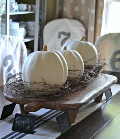 a wooden stand with white pumpkins covered with vine is a rough rustic decoration or centerpiece