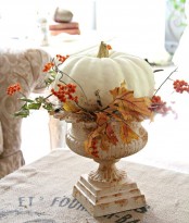 a large white pumpkin with faux berries and leaves placed into a white vintage urn as a pumpkin stand is chic