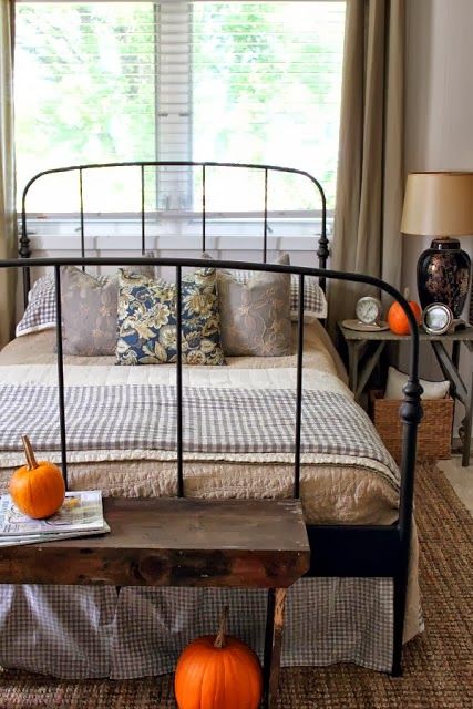 a cozy farmhouse bedroom with wicker rugs and boxes for storage, with a metal bed and a wooden bench 