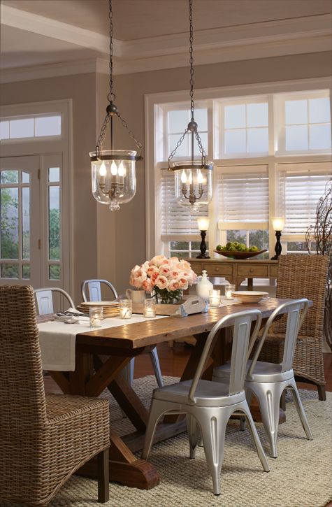 a farmhouse meets glam dining space with a wooden table, metal and wicker chairs, catchy chandeliers and a wooden sideboard