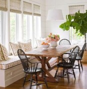 a modern farmhouse dining nook with a windowsill upholstered bench, a wooden table and dark chairs plus wicker shades