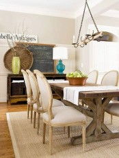 a neutral and welcoming farmhouse dining room with a wooden table, upholstered chairs, a jute rug, a storage unit with baskets and a chalkboard