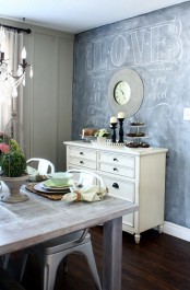 a neutral farmhouse dining room with a chalkboard wall, a white sideboard, whitewashed furniture and a crystal chandelier