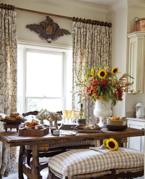 a traditional farmhouse dining space with neutral printed textiles, rich stained wood, rattan benches and bright florals