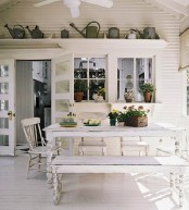 a white farmhouse dining space with shabby chic furniture, watering cans for decor, potted greenery and blooms