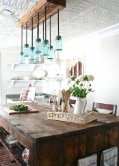 a chic vintage farmhouse dining space with a unique blue jar chandelier, a vintage wooden table and greenery and blooms