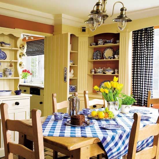 a traditional yellow and blue farmhouse kitchen with checked textiles, built in storage units and a stained dining set