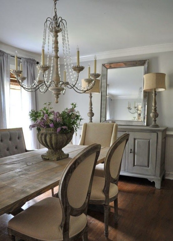 a neutral French farmhouse dining room with a vintage dining set, upholstered chairs, a whitewashed sideboard, vintage lamps and a crystal chandelier