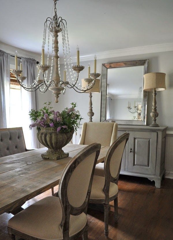 a neutral French farmhouse dining room with a vintage dining set, upholstered chairs, a whitewashed sideboard, vintage lamps and a crystal chandelier