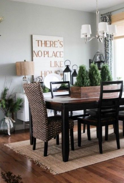 a modern farmhouse dining room with a dark colored dining set, a wicker chair, a sign and some greenery arrangements