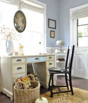 a vintage farmhouse home office with pastel blue walls, a shabby chic desk, a dark chair, vintage artworks and baskets with pumpkins for fall decor