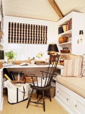 a neutral and cozy farmhouse home office with a built-in desk, bookshelves and a daybed, a vintage chair, a black lamp and a plaid curtain