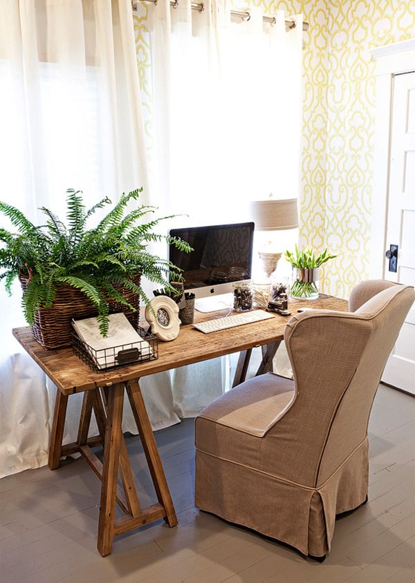a farmhouse home office with yellow printed wallpaper, a wooden desk and a burlap upholstered chair, potted greenery