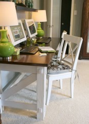 a modern farmhouse home office in neutrals, with a wooden desk with a black tabletop, a chair, green table lamps and some decor on the dark shelf