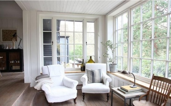 a white farmhouse sunroom nook with vintage furniture, stacks of books and potted greenery is very welcoming