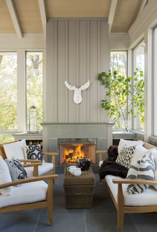 a farmhouse sunroom nook with a fireplace, wooden furniture with white upholstery, greenery and a skull
