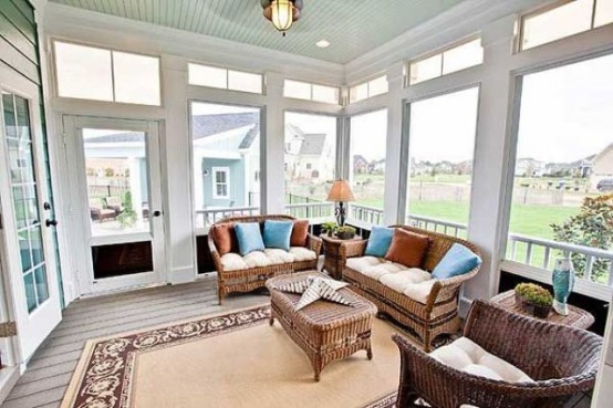 a farmhouse sunroom with rattan furniture, a rug, lamps and bright pillows that make the space more welcoming