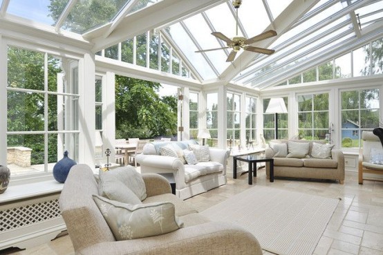 a large neutral farmhouse sunroom with neutral furniture, pendant lamps and some tables is a cool salon for guests