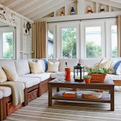 a cozy farmhouse sunroom with wicker furniture, neutral upholstery, orange and blue accessories and lots of large succulents