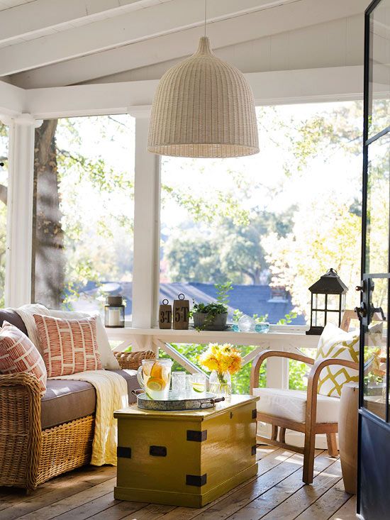 a neutral farmhouse sunroom with wooden and rattan furniture, bright printed pillows and candle lanterns and blooms is very inviting