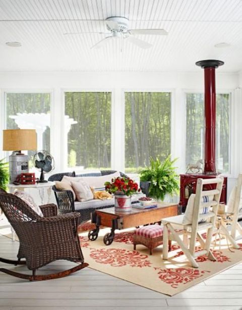 a rustic industrial sunroom with a red hearth, rattan and wooden furniture, a wooden table on casters and some potted greenery and blooms