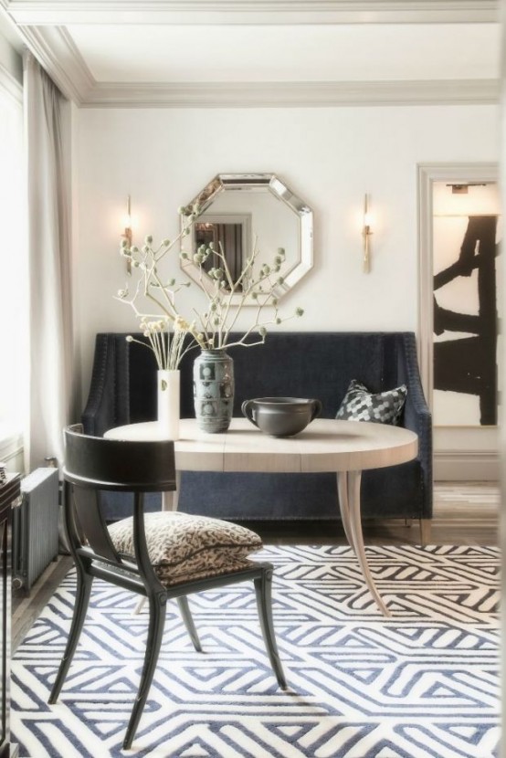 a black and white art deco-inspired dining space with a black sofa, a catchy dining table, a chair, a geometric floor and a geometric mirror on the wall