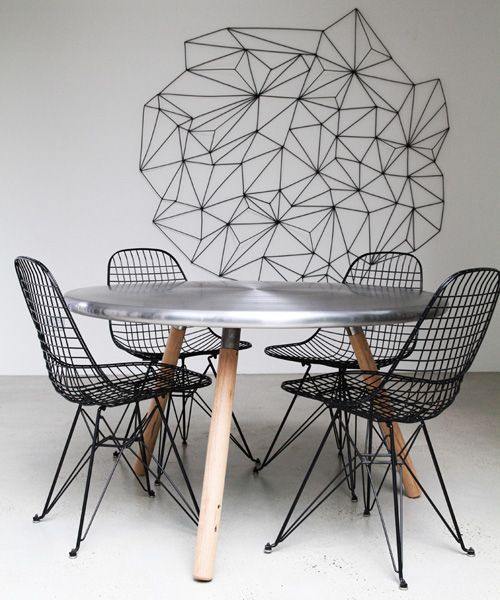 a pretty dining space with geometric decor on the wall, a round table with a metal tabletop, black metal chairs is a lovely and very laconic space to be in