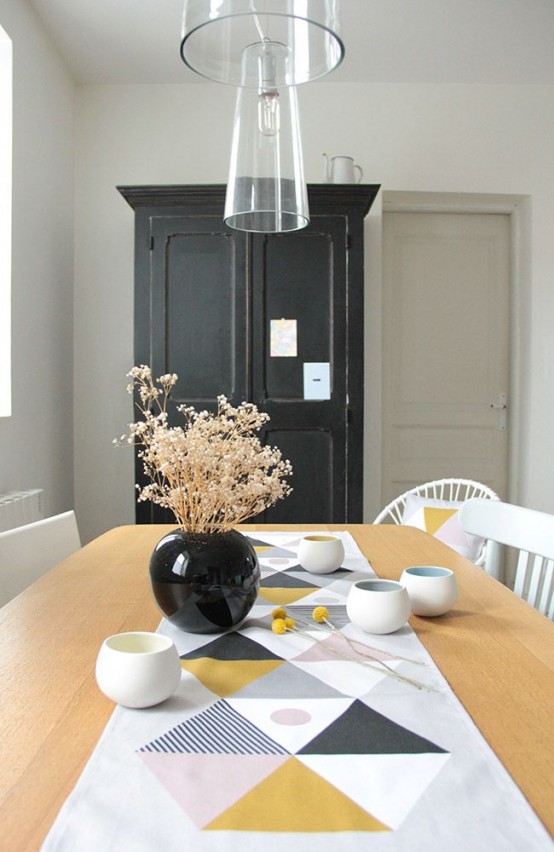 a Scandinavian dining room with a black storage unit, a stained table and white chairs, a geometric table runner, glass pendant lamps and dried branches in a black vase