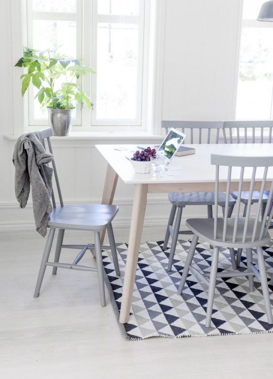 a Nordic dining space with a stained table, a geometric print rug, grey chairs, pendant lamps and some greenery