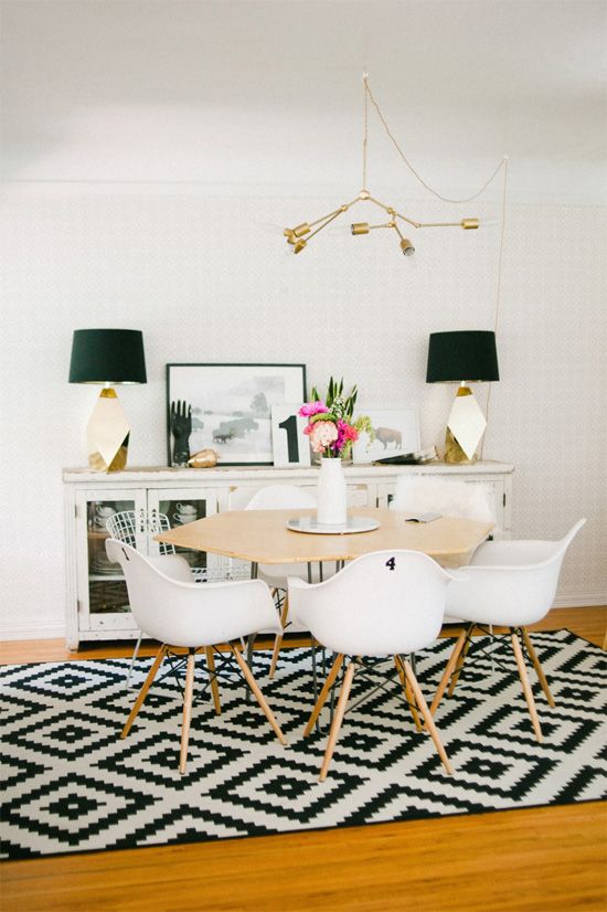 a Scandinavian dining room with a black and white geo rug, a white sideboard and chairs, a geo-shaped dining table, faceted table lamps