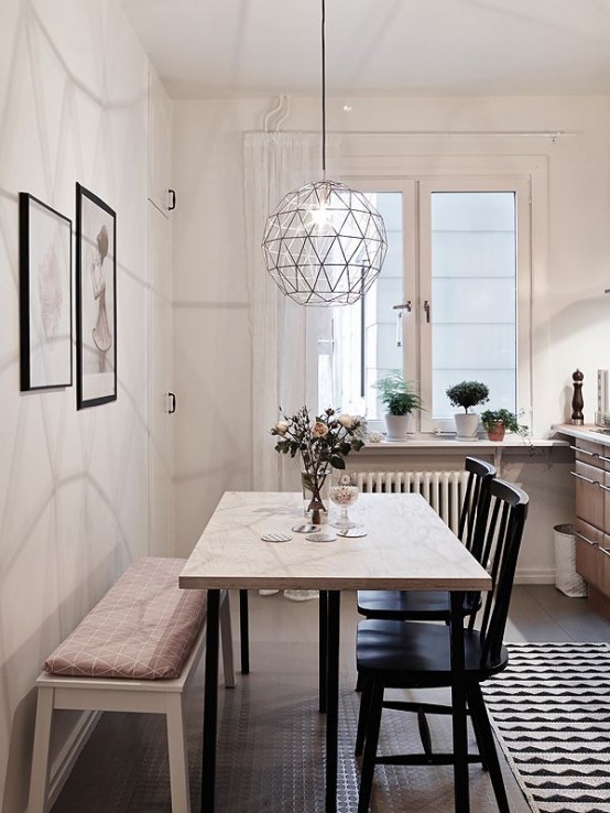 a Scandinavian dining space with a light-stained table, black chairs, a bench with a geometric cushion and a geometric pendant lamp