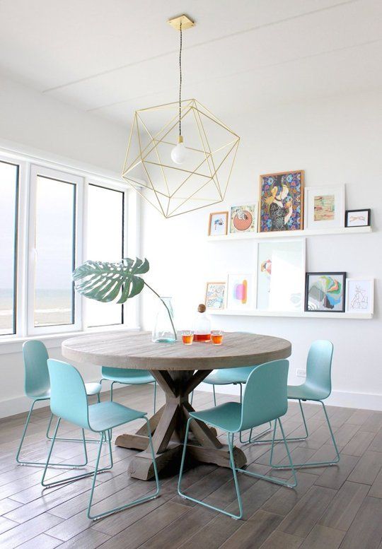 a lovely dining room with a ledge gallery wall, a round wooden dining table, blue chairs and a geometric pendant lamp
