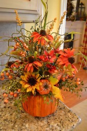 a bright fall centerpiece of a faux pumpkin, bright faux blooms, greenery, berries and various fall stuff for cozy traditional fall decor