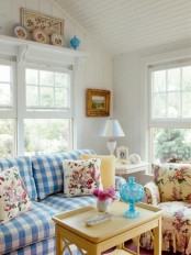 a cottage living room with a blue plaid sofa, a floral chair and matching floral pillows on the sofa, a coffee table with vases and decorative plates