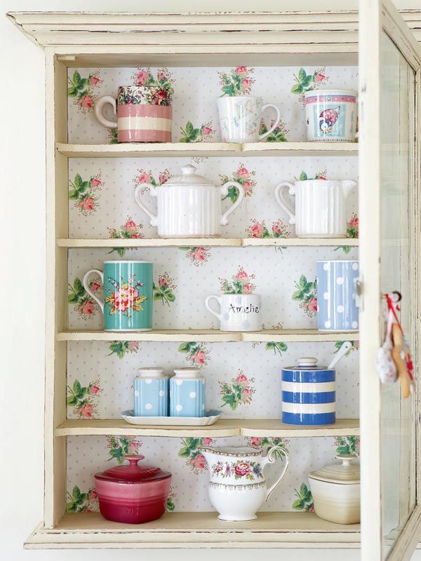 a neutral vintage cabinet with floral wallpaper backing, neutral shelves and vintage tableware on display