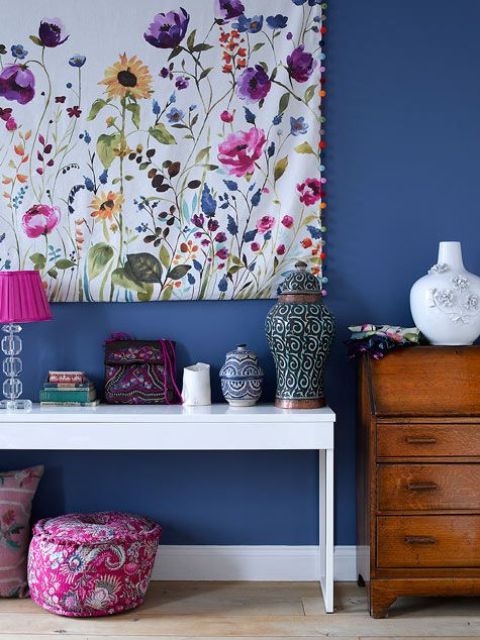 a bold entryway with a navy wall, a stained dresser, a white console table with a lamp and vases, a statement and bold floral artwork