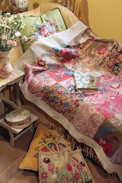 a small cottage bedroom with buttermilk walls, a bed with bold floral bedding and pillows, stools and side tables and blooms