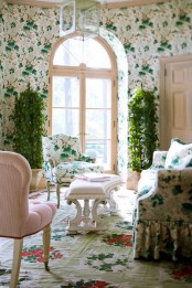 a gorgeous English cottage living room with floral wallpaper walls, matching floral seating furniture, a floral rug and tall plants in pots