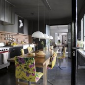 a moody grey and black kitchen with neutral cabinets, a large wooden table and bold floral chairs that add color to the space