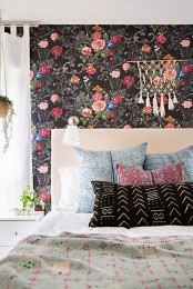 a boho bedroom with a black floral accent wall, a bed with neutral and printed bedding, macrame, potted plants