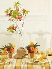 bright fall or Thanksgiving centerpieces of orange and burgundy blooms, succulents and berries and a burlap sack with a small tree with fall leaves