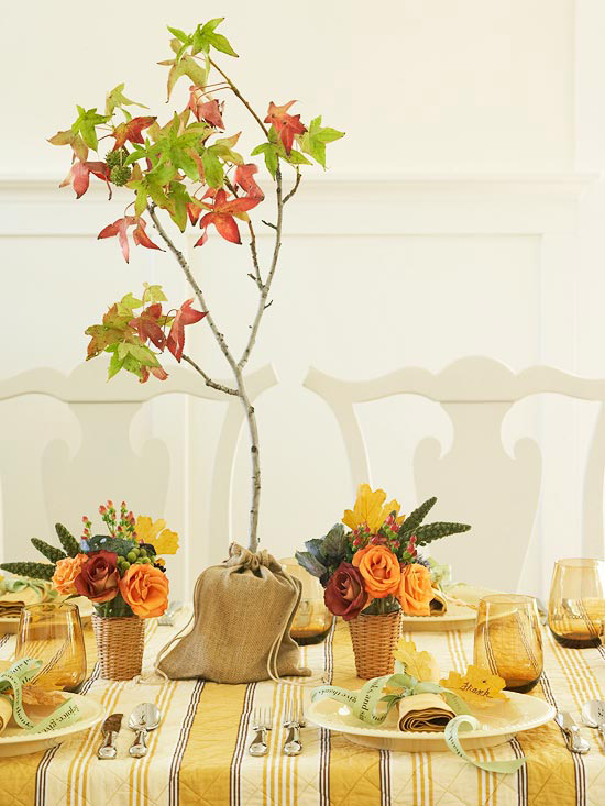 bright fall or Thanksgiving centerpieces of orange and burgundy blooms, succulents and berries and a burlap sack with a small tree with fall leaves