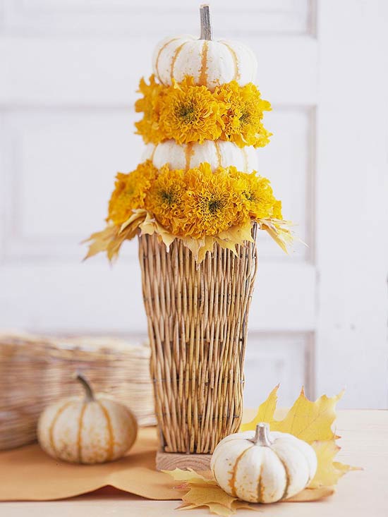 a catchy rustic Thanksgiving centerpiece of a woven basket with yellow blooms and leaves and a couple of stacked white pumpkins is a catchy idea