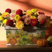 a colorful fall or Thanksgiving centerpiece of a box with painted pumpkins and yellow, burgundy, pink blooms is a gorgeous idea