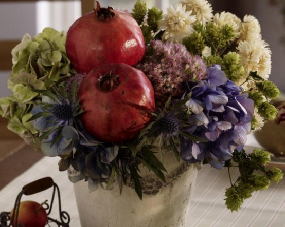 a bold fall or Thanksgiving centerpiece of a bucket, white, pink, green and purple blooms and pomegranates is a very catchy and decadent idea