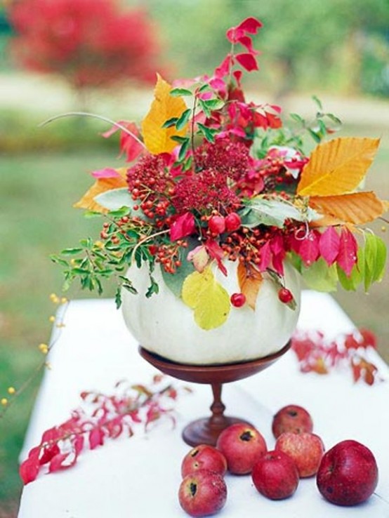 a bright and cool Thanksgiving centerpiece of a white pumpkin, bold leaves and green ones, bright blooms, berries on a wooden stand is a cool centerpiece idea