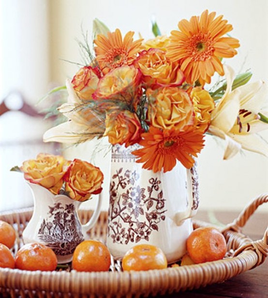 a bold fall or Thanksgiving centerpiece of a woven tray with citrus, orange blooms in jugs and vases is a lovely idea with a touch of color